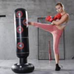 Boxeuseuse blonde portant un legging rose, est en train de s'entrainer sur un sac de boxe gonflable noir avec des cibles rouges, ses gants sont rouges et elle se trouve dans une salle en béton