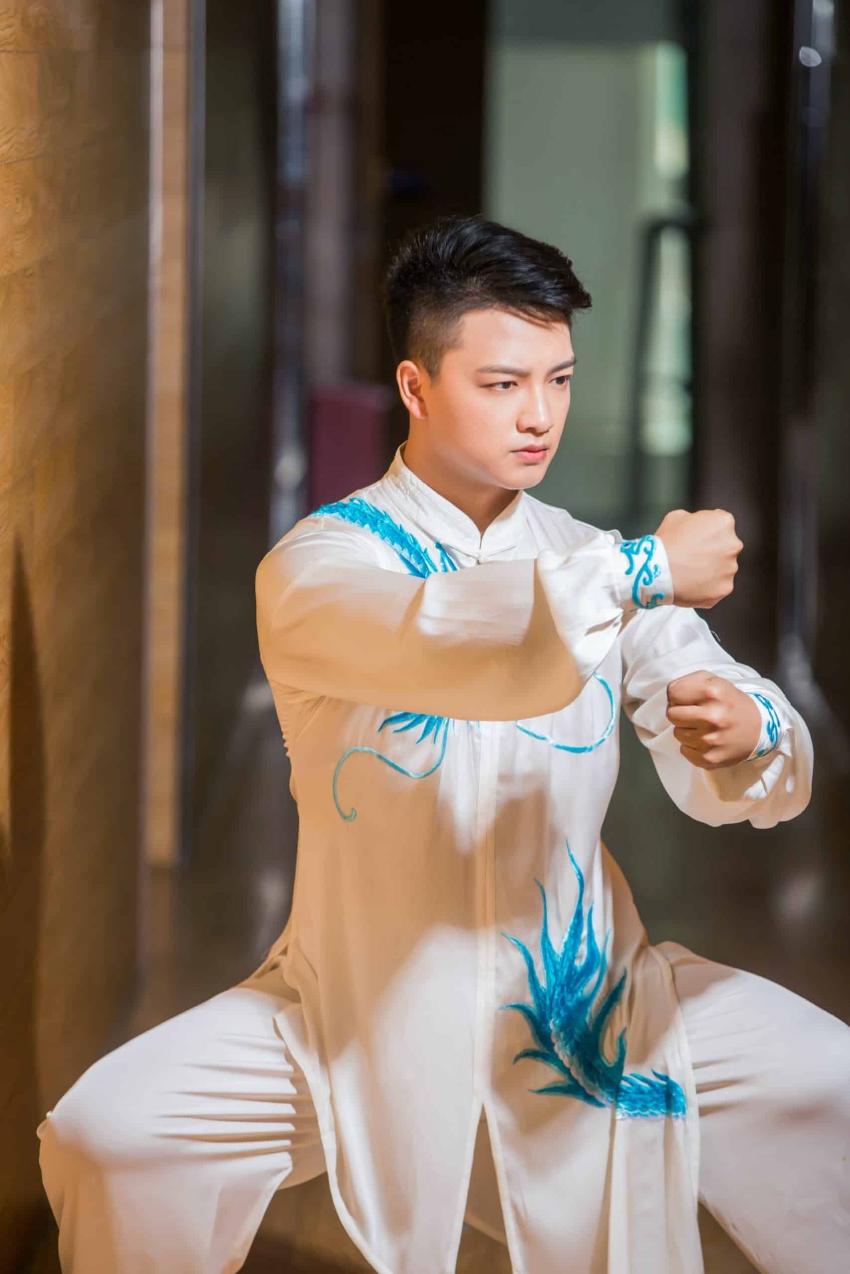 Homme en train de pratiquer le Tai-Chi dans une tenue blanche avec des broderie bleu turquoise