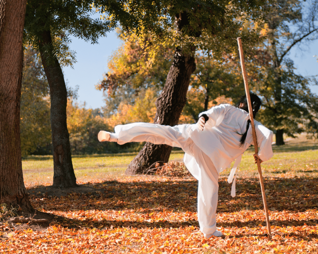 Personne pratiquant le kung fu dans un parc avec un baton et une tenue blanche