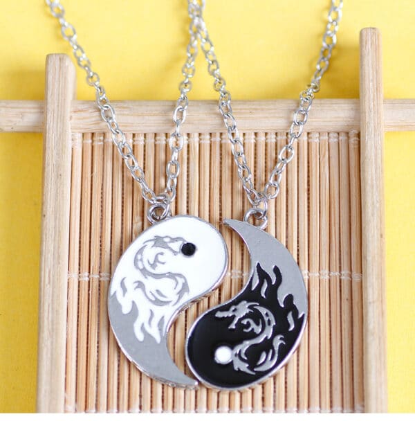 collier de couple de tai chi , ying et yang, représentant un dragon sur chaque partie, posés sur un support en bois fin
