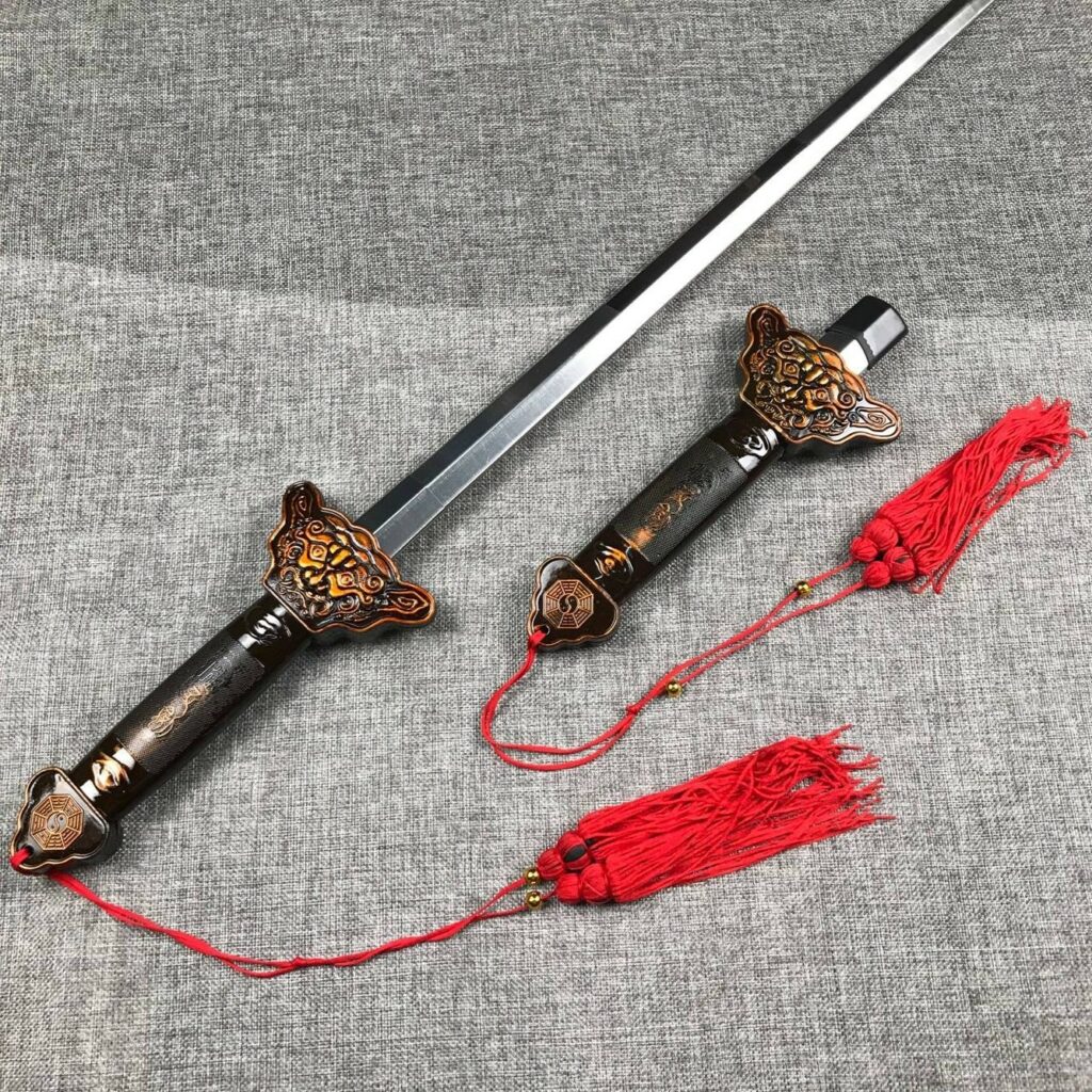 épée à lame extensible pour arts martiaux, avec décoration rouge est posée à plat sur un matériau gris