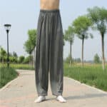 personne dont on ne voit que les jambes porte un pantalon ample d'arts martiaux gris et se tient debout au milieu de l'allée d'un parc