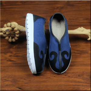 paires de chaussures d'arts martiaux, bleues avec motif noir, et semelle blanche, une des chaussures est présentée à plat et l'autre sur le côté, elle sont appuyées sur un morceau de bois