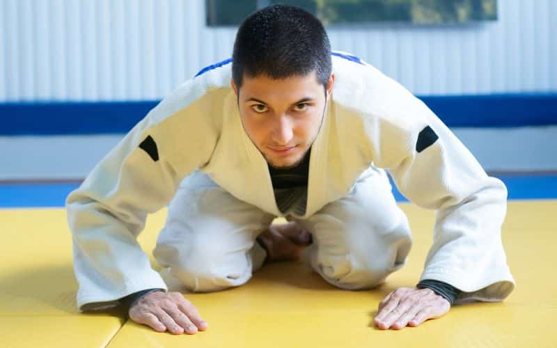 Homme en kimono de judo, en position de salut sur un tatami jaune.