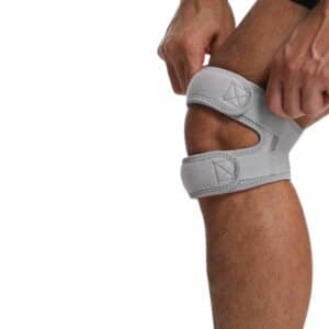 Genouillère Grappling Réglable Double Support mise sur un grise mise sur genoux d'un homme sur fond blanc