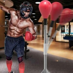 Punching Ball Sur Pied Rouge pour Travail de Vitesse avec homme qui porte un casque de boxe qui frappe dedans dans une salle de sport